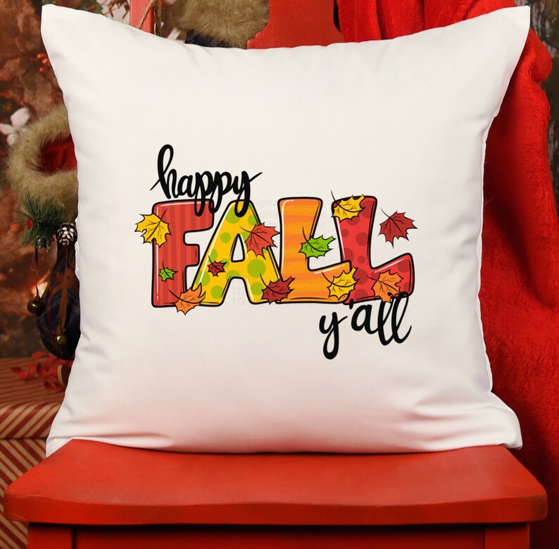 May include: A white square pillow with the words "happy FALL y'all" in black script. The word "FALL" is in colorful letters with fall leaves. The pillow is on a red surface.