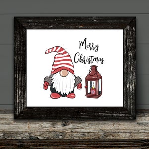 May include: A framed print featuring a Christmas gnome with a red and white striped hat, a white beard, and red mittens. Beside the gnome is a red lantern with a lit candle. The words "Merry Christmas" are written above the gnome.
