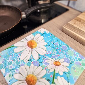 May include: A blue and white floral print kitchen trivet with white daisies and pink and blue bubbles. The trivet is made of a heat-resistant material and is perfect for protecting worktops from hot dishes.