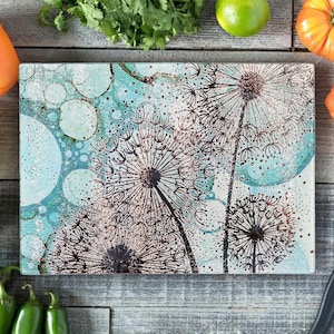 May include: A rectangular glass chopping board with a blue and white background featuring a black and white dandelion design.