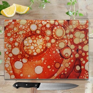 May include: Orange and gold glass chopping board with a circular pattern. The board is made of tempered glass and is heat resistant.