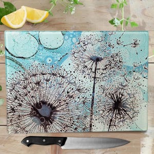 May include: A glass chopping board with a blue and white background featuring a black and white dandelion design.