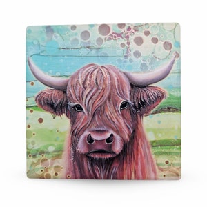 Op de afbeelding: Vierkante kunstdruk met een Schotse Hooglander met lange, roodbruine vacht en grote hoorns. De achtergrond heeft een blauwe lucht en een groen veld met abstracte, belachtige vormen. Het gezicht van de koe is de focus.