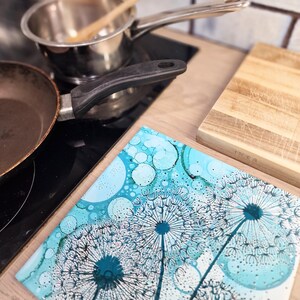 May include: A blue and white glass trivet with a dandelion design. The trivet is on a wooden surface.