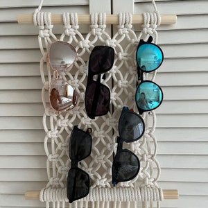 以下が含まれることがあります： マクラメの壁掛けに、5つのサングラスが掛けられています。サングラスは、黒、茶色、青など、さまざまな色とスタイルがあります。