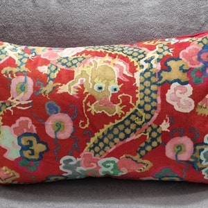 Puede incluir: Almohada roja con un diseño de dragón dorado y azul. El dragón está rodeado de nubes rosas, azules y verdes.