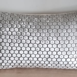 May include: A rectangular decorative pillow with a repeating honeycomb pattern. The pillow features a light gray and dark gray color scheme. The pillow is made of a soft, textured fabric and is designed for home decor.