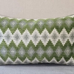 Puede incluir: Una almohada rectangular verde y gris con un diseño geométrico. La almohada es suave y tiene una textura mullida.
