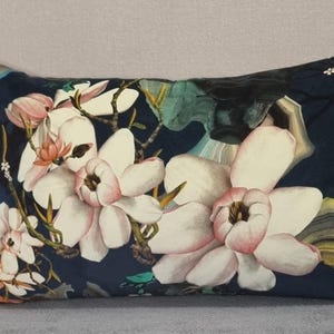 May include: A navy blue throw pillow with a floral design featuring large white magnolia flowers with pink centers. The flowers are arranged on a dark blue background with hints of green and yellow.