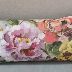 Könnte beinhalten: Ein rechteckiges Zierkissen mit einem malerischen Blumenmuster, das große rosa, gelbe und korallenfarbene Blüten auf einem gedämpften grauen Hintergrund zeigt. Das Design weist sichtbare Pinselstrichstrukturen und grüne Blattakzente auf.