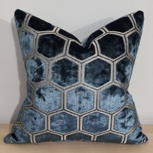 Könnte beinhalten: Ein quadratisches Zierkissen mit einem geometrischen Wabenmuster. Das Kissen hat eine weiche, samtartige Textur in Blau- und Türkistönen. Das Wabenmuster ist mit einer silbergrauen Naht umrandet, was der Oberfläche des Kissens einen Kontrast verleiht.