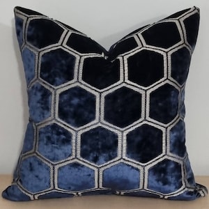 Puede incluir: Un cojín decorativo cuadrado con un patrón geométrico de panal. El cojín presenta un degradado de tonos azules, que transicionan de un tono más claro a un azul marino profundo. El diseño de panal está delineado con hilo gris plateado.
