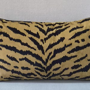 May include: Rectangular cushion with a tiger stripe pattern. The cushion has a tan background with black stripes. It has a black border and is placed on a light blue surface.