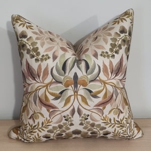 Puede incluir: Una almohada decorativa con un patrón floral en tonos marrones, verdes y beige. La almohada presenta un diseño simétrico con detalles intrincados.