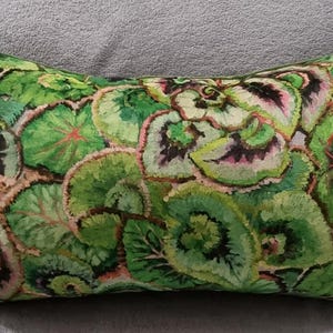 May include: Rectangular decorative pillow featuring a vibrant botanical pattern. The pillow showcases a detailed design of green leaves with accents of pink and black, set against a light background. The pillow is a home decor item.