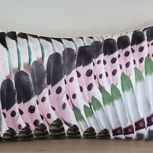 Peut inclure: Coussin décoratif rectangulaire avec un motif de plumes. Le coussin présente un motif répété de plumes stylisées dans des tons de noir, blanc, rose et vert. Les plumes ont un motif à pois et sont disposées en forme incurvée.
