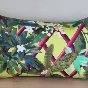 Puede incluir: Una almohada verde y rosa con un patrón floral. La almohada presenta un diseño de enrejado con enredaderas rosas y flores blancas. El fondo es de color verde brillante.