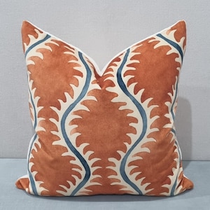 May include: Square decorative pillow with a repeating pattern of rust-colored leaf-like shapes and blue wavy lines on an off-white background. The pillow has a white border and is likely used for home decor.