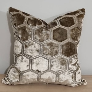 Puede incluir: Una almohada de terciopelo beige con un patrón de panal. La almohada es suave y mullida, y el patrón de panal es sutil y elegante.