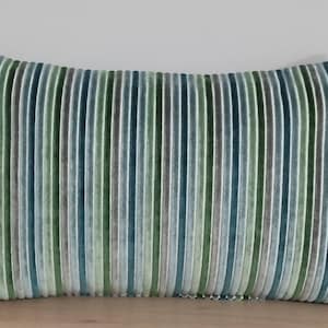 Puede incluir: Una almohada rectangular larga con un patrón de rayas en tonos de verde, azul y gris. La almohada está hecha de una tela suave y aterciopelada.