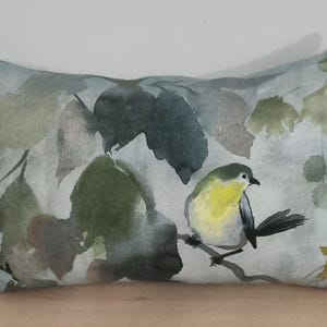 May include: Decorative rectangular pillow featuring a watercolor painting of a small yellow and green bird perched on a branch. The background has a soft, muted green and gray leaf pattern.