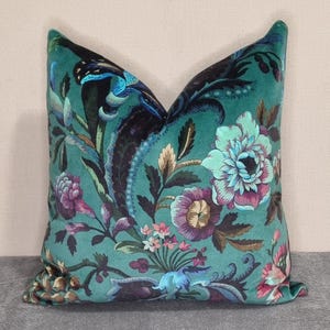 May include: A decorative throw pillow with a teal background and a floral pattern. The design features large flowers in shades of purple, pink, and teal, with dark blue and black accents. The pillow has a soft, velvety texture.