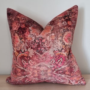 Könnte beinhalten: Ein rotes, rosa und orangefarbenes Dekokissen mit einem floralen Muster. Das Kissen ist aus einem weichen, samtigen Stoff.