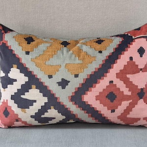 May include: A rectangular throw pillow featuring a geometric pattern with diamond and chevron shapes. The design incorporates a color palette of dark charcoal, muted mustard yellow, soft light blue, and dusty rose pink across the fabric surface.