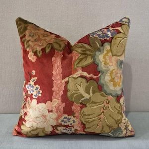 May include: A decorative throw pillow with a floral pattern. The pillow features a red background with large, stylized flowers in shades of cream, green, and blue. The pillow has a soft, velvety texture and is square-shaped.