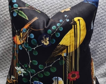 May include: Black pillow with a colorful bird and floral pattern. The birds are yellow, blue, and orange. The flowers are red, blue, and yellow. The background is black.