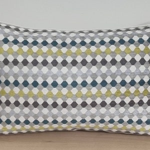 Puede incluir: Una almohada rectangular con un patrón geométrico en tonos grises, azul verdoso y amarillo. El patrón está formado por pequeños hexágonos.