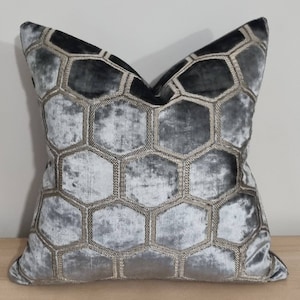 May include: A grey velvet cushion with a geometric pattern of beige hexagons. The cushion is soft and plush, and the pattern is subtle and elegant.