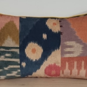 May include: Rectangular cushion with a patchwork design in shades of pink, blue, orange, and green. The cushion has a yellow border. The fabric has a soft, textured appearance. Ideal for adding a touch of colour to a sofa or bed.