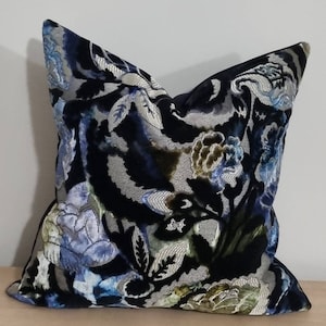 Puede incluir: Una almohada de terciopelo negro con un patrón floral en tonos azules, plateados y verdes. La almohada tiene una forma cuadrada y un borde decorativo.