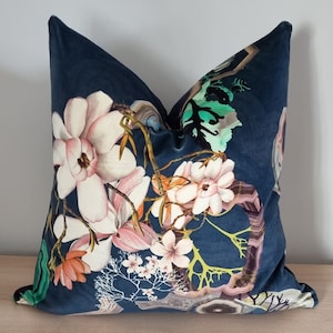 May include: A navy blue decorative pillow featuring a floral design with large, light pink and white magnolia blossoms. The pillow has a velvet texture and includes accents of green, orange, and brown.