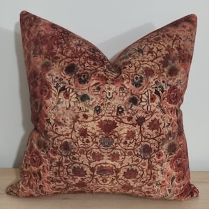 May include: A red, brown, and cream throw pillow with a floral pattern. The pillow is made of velvet and has a soft, luxurious feel.