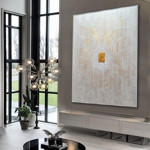 May include: A large rectangular wall art piece featuring a white textured surface with intricate, raised wavy lines and gold accents. A solid, square gold-leaf element is positioned in the centre of the canvas, creating a focal point.