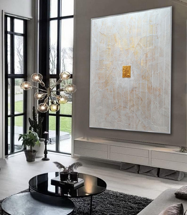 May include: A large rectangular wall art piece featuring a white textured surface with intricate, raised wavy lines and gold accents. A solid, square gold-leaf element is positioned in the centre of the canvas, creating a focal point.