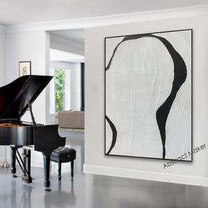 May include: A large, abstract painting with a black frame. The artwork features a textured white background with bold, black, organic shapes. The painting hangs on a white wall, next to a black grand piano and a black piano bench.
