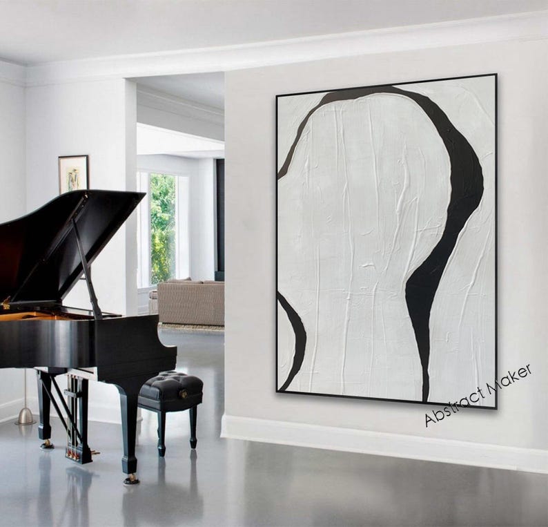 May include: A large, abstract painting with a black frame. The artwork features a textured white background with bold, black, organic shapes. The painting hangs on a white wall, next to a black grand piano and a black piano bench.