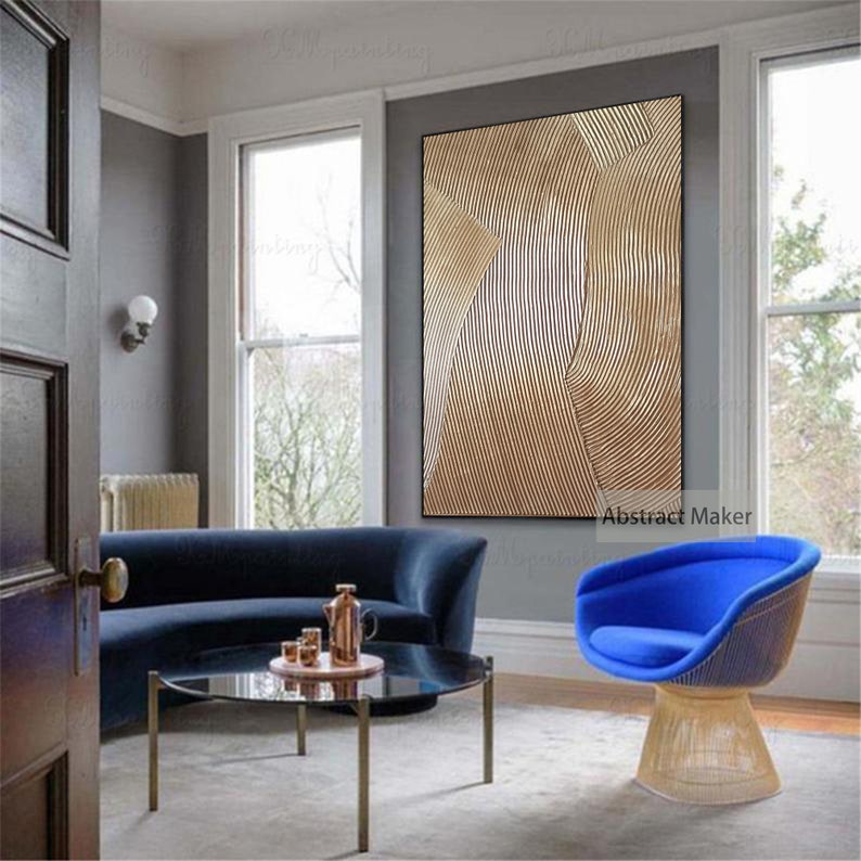 Puede incluir: Un sof&aacute; de terciopelo azul y un sill&oacute;n azul con estructura de metal dorado se encuentran en una sala de estar con una pintura abstracta dorada y blanca en la pared. La pintura tiene el texto "Abstract Maker" en la parte inferior.