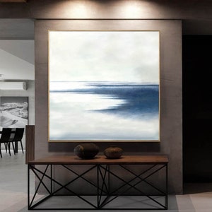 May include: An abstract painting with a gold frame depicts a seascape in shades of blue and white. The artwork hangs above a wooden console table with a black metal base. Two decorative ceramic vases sit on the table.
