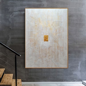 May include: A large rectangular wall art piece featuring a white textured surface with raised wavy lines and gold accents. In the centre, two small, rectangular, gold-leafed panels are positioned side-by-side, framed in a thin gold border.