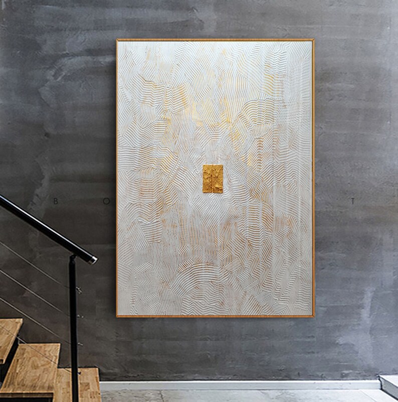 May include: A large rectangular wall art piece featuring a white textured surface with raised wavy lines and gold accents. In the centre, two small, rectangular, gold-leafed panels are positioned side-by-side, framed in a thin gold border.