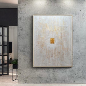 May include: A rectangular wall art piece featuring a white textured surface with intricate, wavy, embossed lines and subtle gold accents. A small, solid gold-coloured rectangular element is positioned in the centre of the canvas, framed in a thin gold border.
