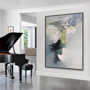 May include: Abstract painting in shades of gray, green, and white with thick brushstrokes and a textured surface. The painting is framed in black and hangs on a white wall in a modern interior.