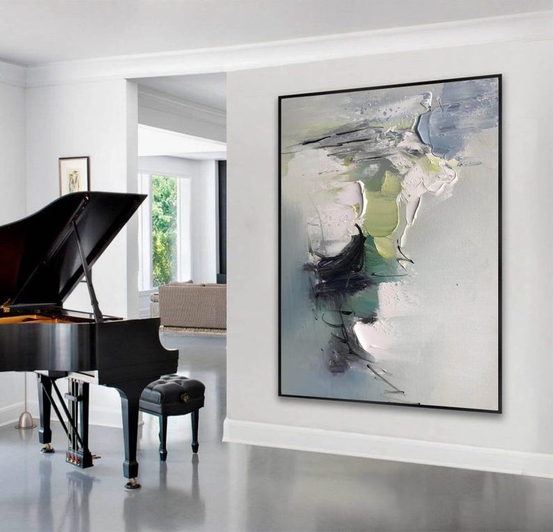 May include: Abstract painting in shades of gray, green, and white with thick brushstrokes and a textured surface. The painting is framed in black and hangs on a white wall in a modern interior.
