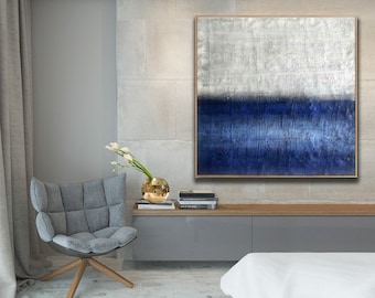 Puede incluir: Pintura abstracta con un esquema de color blanco y azul. La mitad superior de la pintura es blanca con una superficie texturizada. La mitad inferior de la pintura es de un azul profundo con pinceladas horizontales. La pintura está enmarcada en un marco fino de oro.