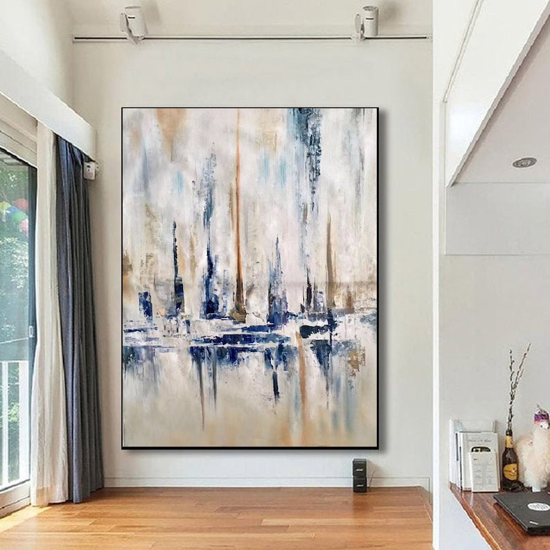 May include: Abstract painting with a black frame. The artwork features vertical brushstrokes in shades of blue, white, and beige, creating a textured effect. The lower portion of the painting has a reflective quality, suggesting a water or mirror-like surface.