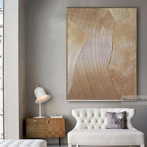 Puede incluir: Impresi&oacute;n de arte abstracto con un patr&oacute;n geom&eacute;trico marr&oacute;n y blanco. La impresi&oacute;n est&aacute; enmarcada en un marco dorado fino y cuelga de una pared gris claro sobre un sof&aacute; blanco.